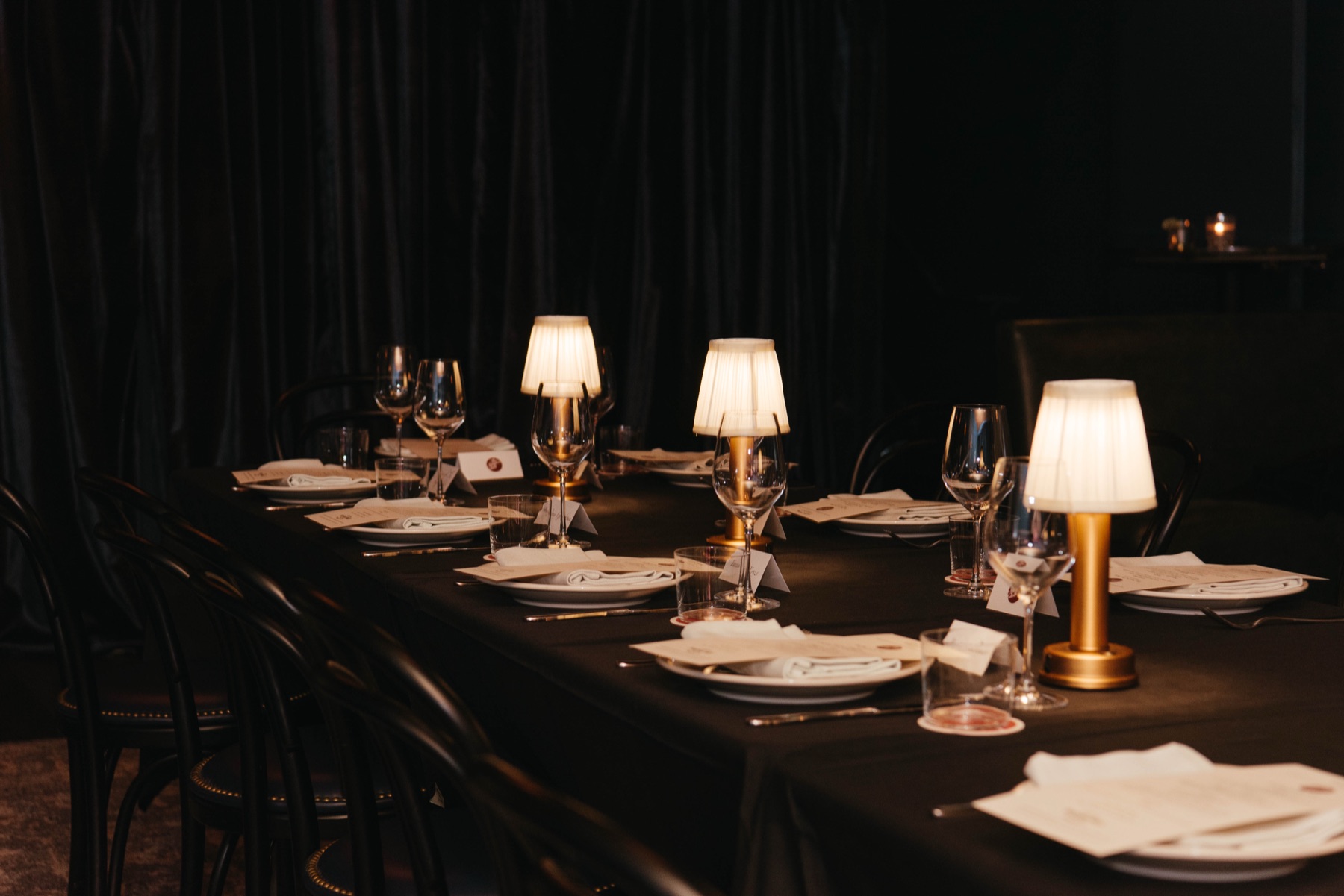 A table set and lit, brass lamps running its length before the guests arrive